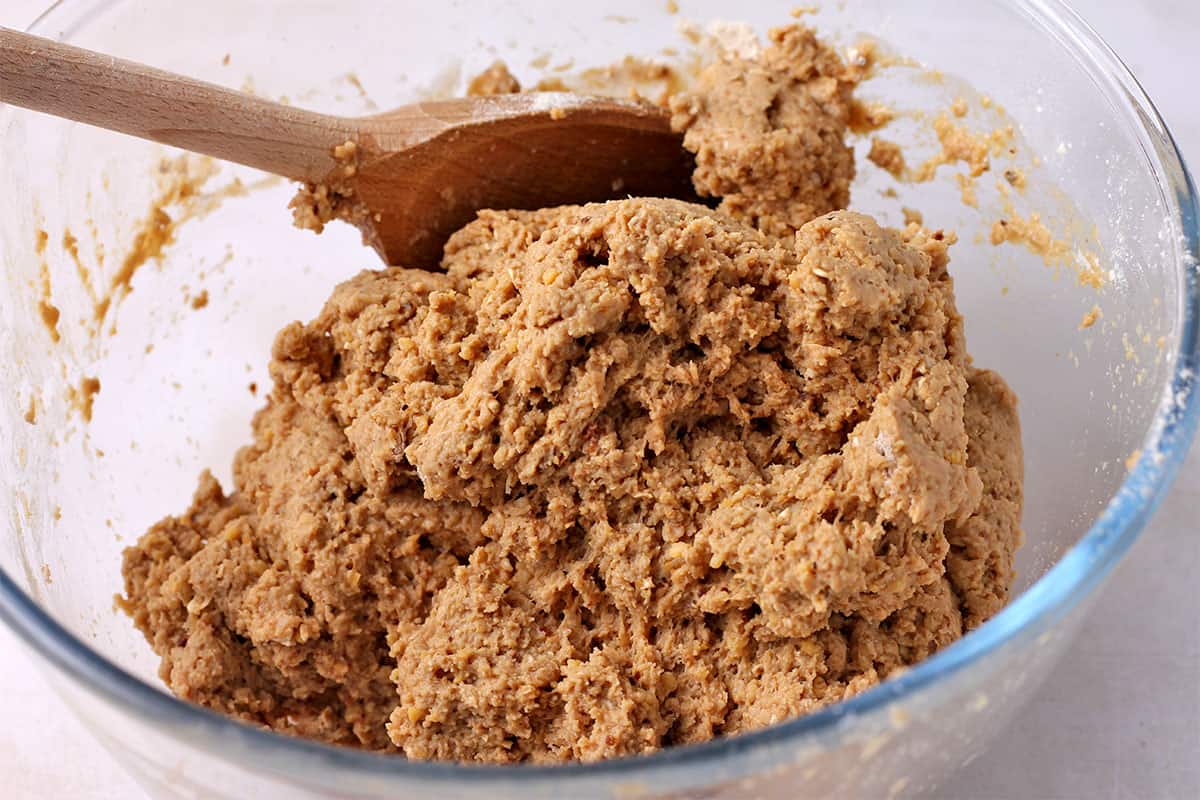 Seitan dough in a glass bowl is mixed with a wooden spoon.