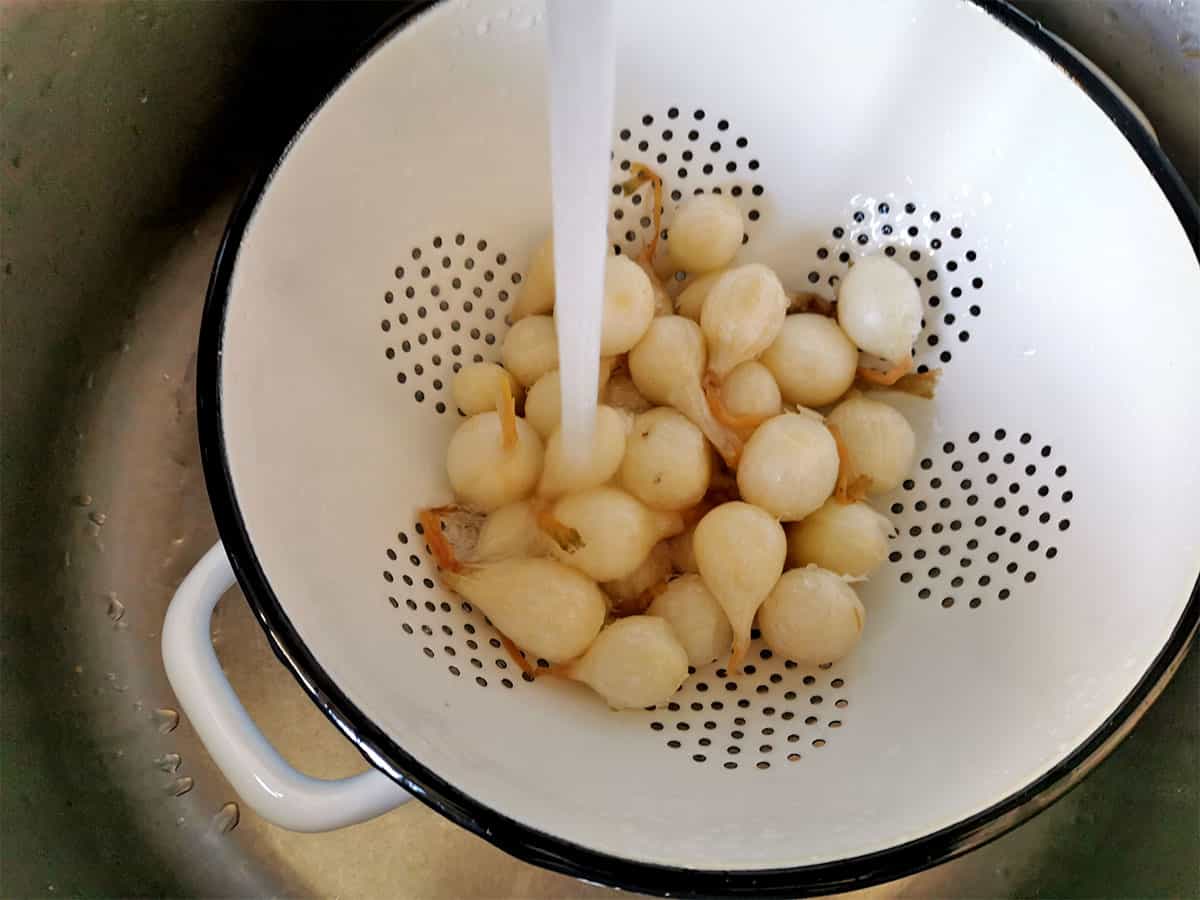 Pearled onions in a white colander are rinsed.