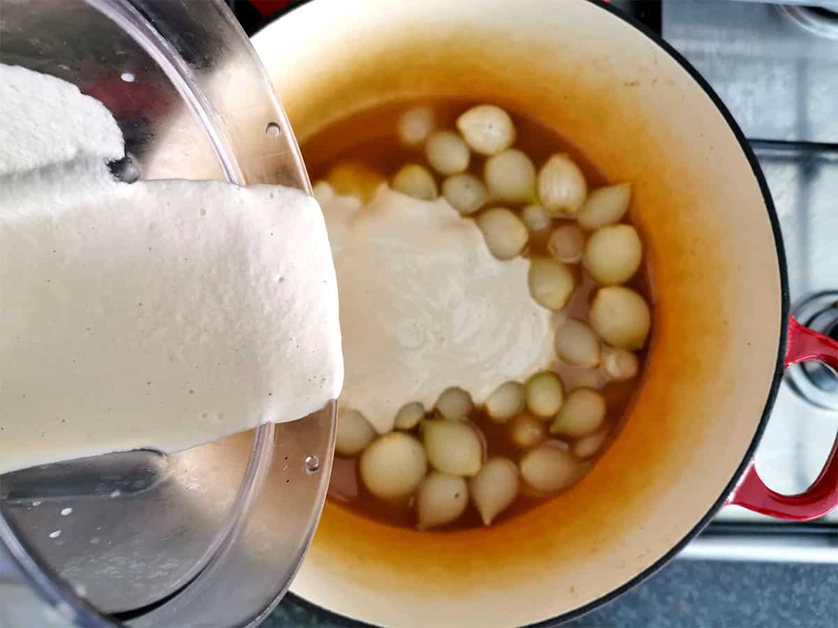 Cashew cream sauce is added to pearled onions in broth.