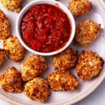 Breaded cauliflower bites with a bowl of marinara dipping sauce on a plate.