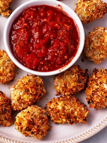 Breaded cauliflower bites with a bowl of marinara dipping sauce on a plate.