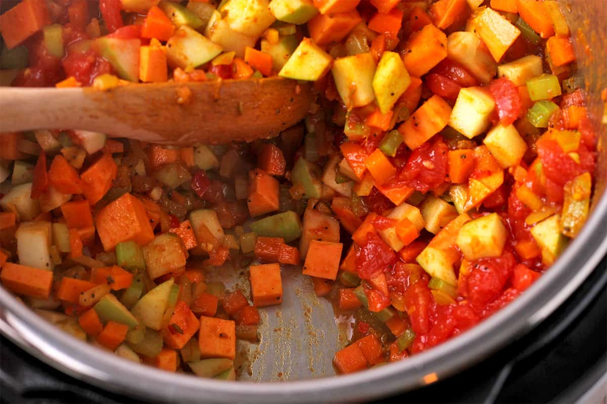 Vegetables and tomatoes are stirred with a wooden spoon in the Instant Pot.