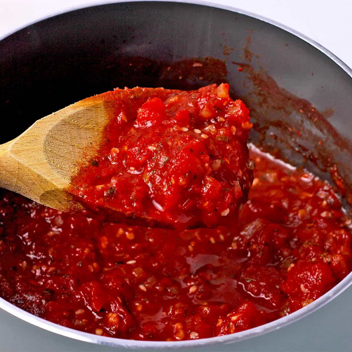 A wooden spoon with marinara dipping sauce held over a saucepan.