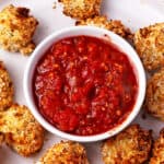 Marinara dipping sauce in a bowl surrounded by roasted cauliflower with panko.