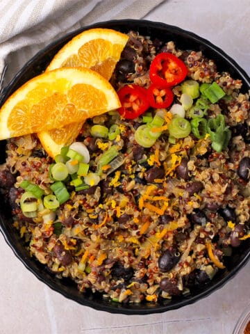 A bowl of tri color quinoa with black beans, orange slices and zest and sliced red chili.
