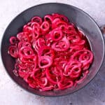 Quick pickled red onion slices in a black bowl.