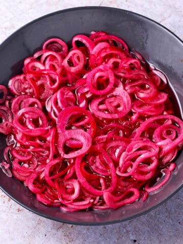 Quick pickled red onion slices in a black bowl.