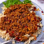 Vegan fesenjan with lentils, walnuts, and pomegranate seeds on a plate over rice.