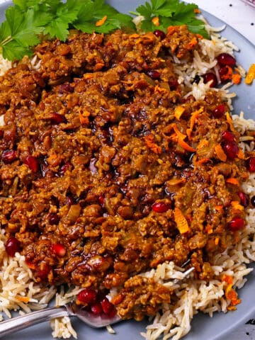 Vegan fesenjan with lentils, walnuts, and pomegranate seeds on a plate over rice.