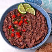 Refried black beans with lime slices in a blue bowl.