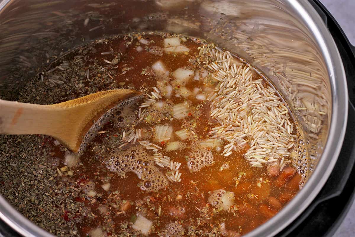 Rice, pinto beans, broth, onions, and oregano is stirred in the Instant Pot.