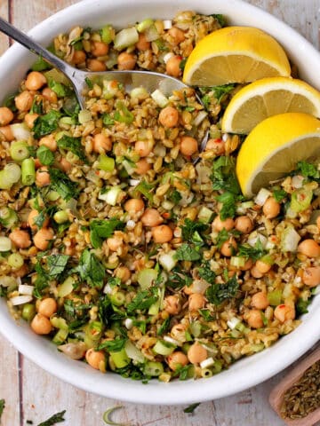 A white bowl with freekeh salad with chickpeas, green onions, and chopped herbs.