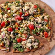 Quinoa crust salad pizza with white beans, veggies, and vegan parmesan on a pizza stone.