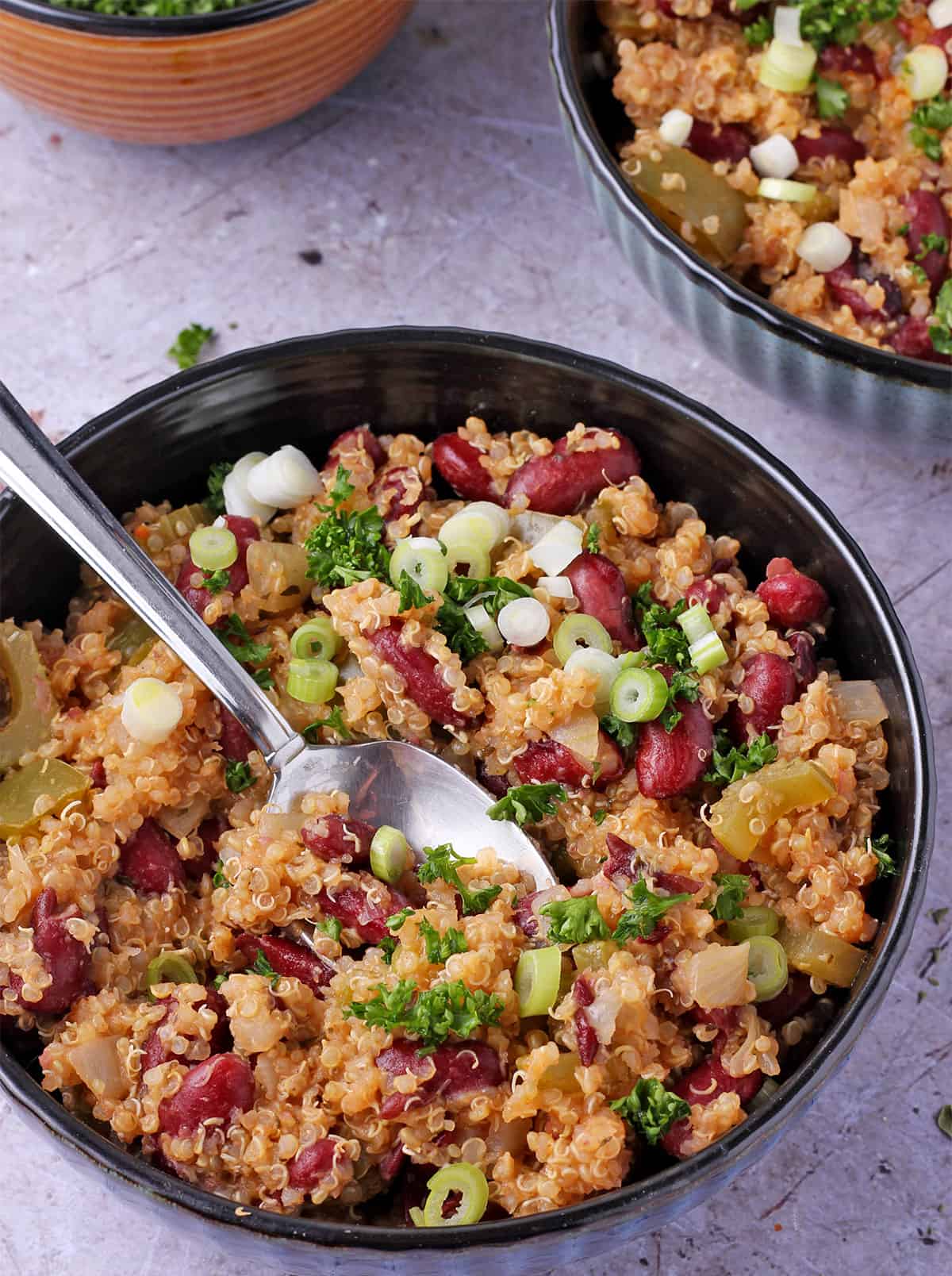 Red beans and quinoa with parsley and green onions in a bowl with a spoon.