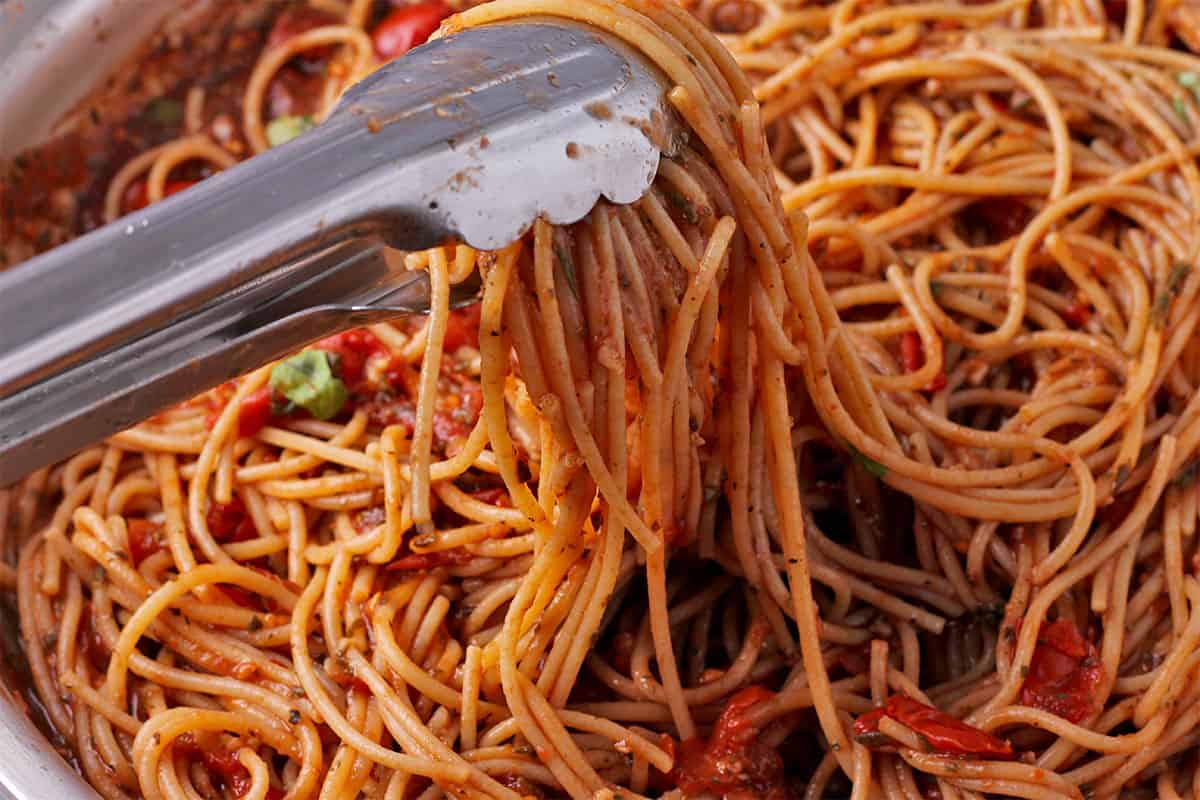 Cooked spaghetti is mixed with arrabbiata sauce.