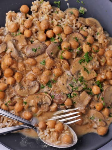 Creamy chickpeas and mushrooms on a plate with rice and a spoon and fork.
