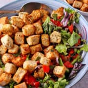 Air fryer croutons over a bowl of lettuce salad.