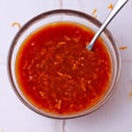 A dish of orange ginger sauce with a spoon.