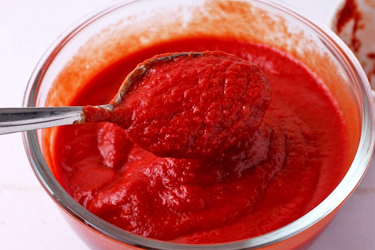 Tomato sauce and tomato paste are mixed with a spoon.