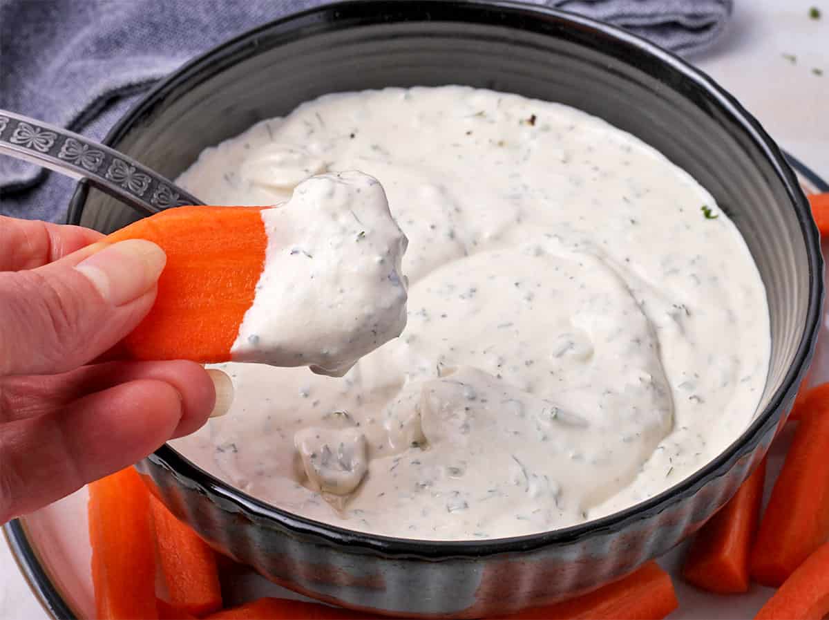 A carrot is dipped into vegan ranch dressing.