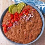A bowl of refried pinto beans with chopped tomatoes, red onions, and lime slices.