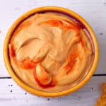 A bowl of cashew queso dip with hot sauce.