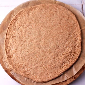 Vegan whole wheat pizza dough on parchment paper and pizza stone.