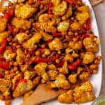 Cauliflower shawarma with chickpeas, red peppers, and red onions on a white plate.