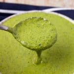 Green tahini sauce lifted in a spoon over a bowl of sauce.