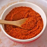 Shawarma spice blend in a red bowl with a wooden spoon.