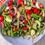 Green bean salad with red onions, cucumber, sliced cherry tomatoes, and dressing in a blue bowl.