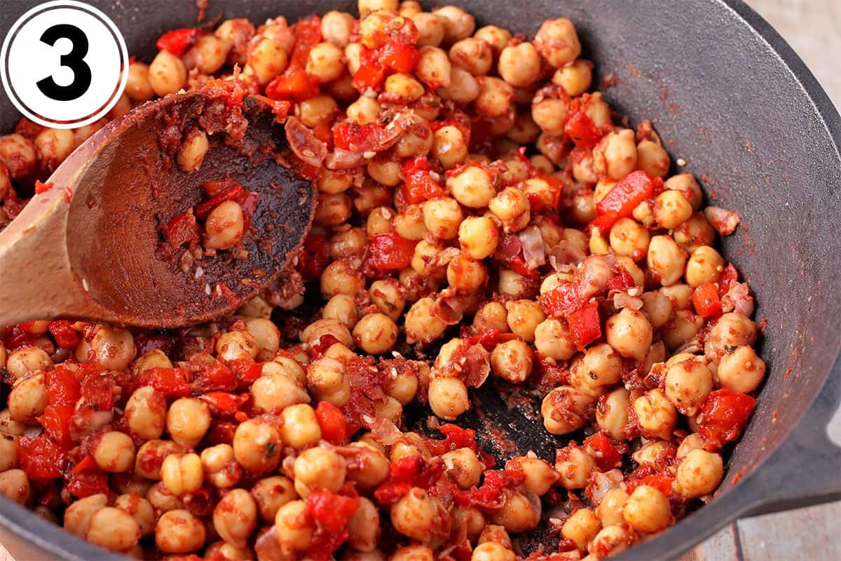 Chickpeas and red pepper are stirred in a pot.