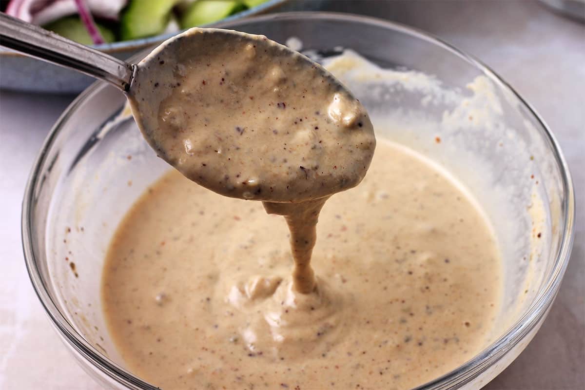 Tahini and za'atar dressing is dripped from a spoon.