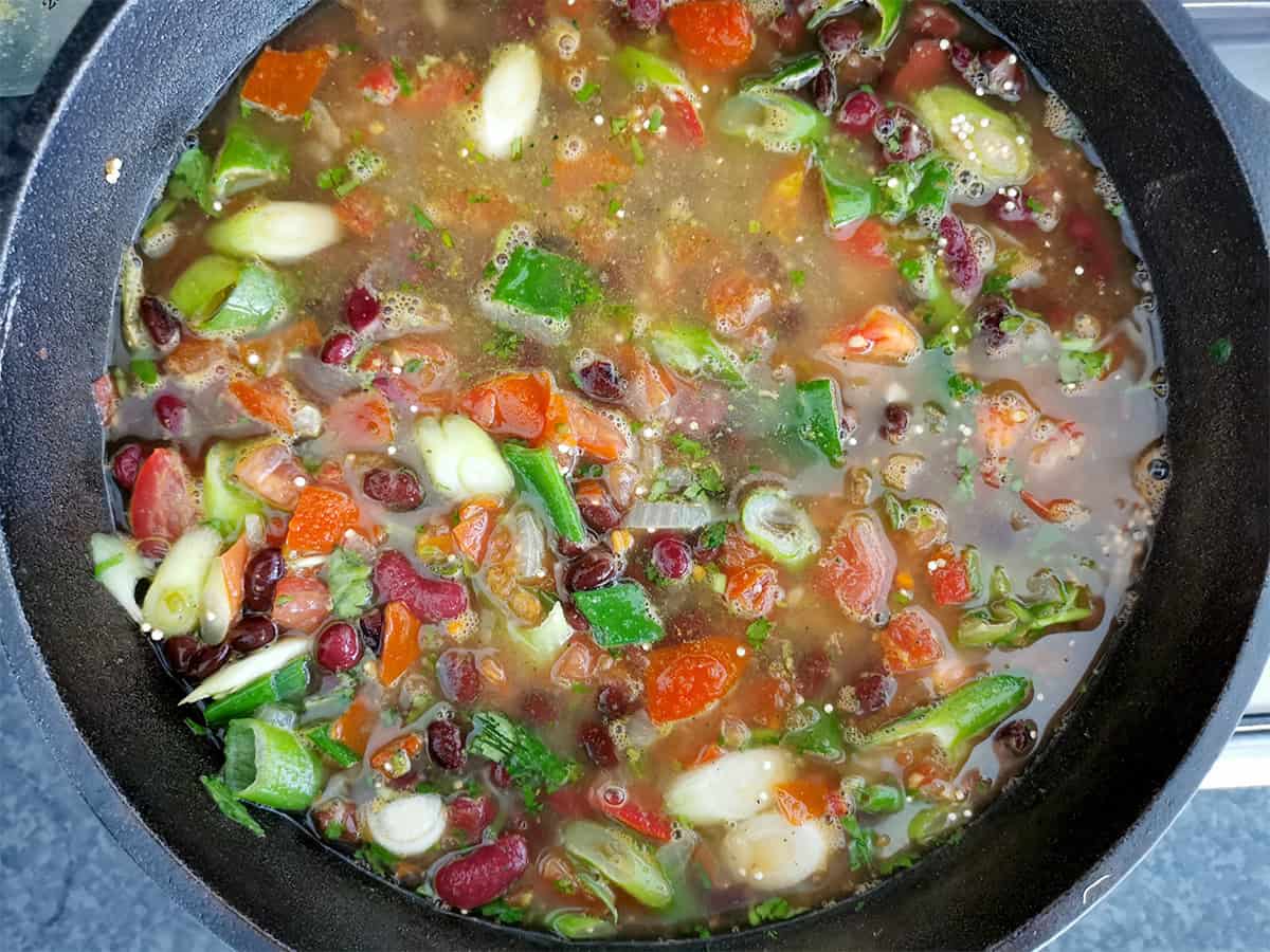 Quinoa, beans, tomatoes, and green onions with vegetable broth in a cast iron pot.