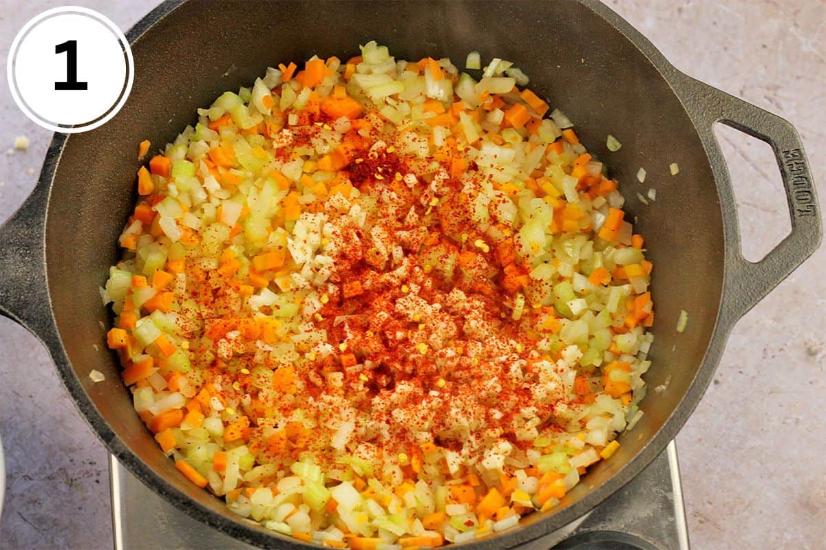 Onions, carrots, and celery in a cast iron pan with paprika over the top.