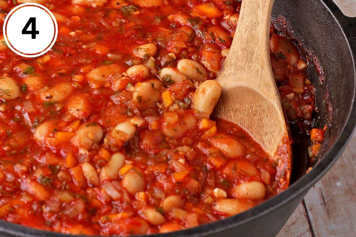 Greek baked beans in a cast iron pan with a wooden spoon.