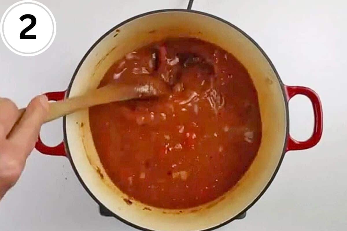 Canned tomatoes and onions are stirred in a pot.