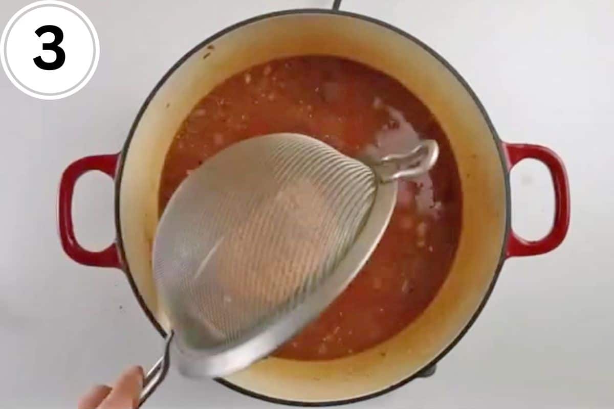 Red lentils from a mesh strainer are added to tomatoes in a pot.