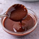 Pomegranate vinaigrette dressing is dripping from a spoon over a glass bowl of dressing.