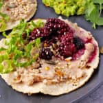 A white refried beans tostada with blackberry salsa, seed mix, and lettuce.