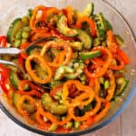 A bowl of cucumber bell pepper salad with edamame and sesame seeds in a bowl with serving spoons.