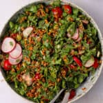 Farro arugula salad with radishes, tomatoes, and vegan parmesan cheese.