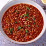 Tomato lentil soup in a bowl topped with chopped parsley and red chili flakes.