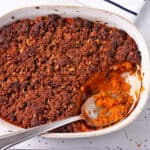 Sweet potato casserole with crumble topping in a baking dish with a spoon.