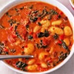 A bowl of gnocchi soup with tomatoes, kale, and white beans.