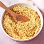 A bowl of vegan parmesan cheese with a wooden spoon.
