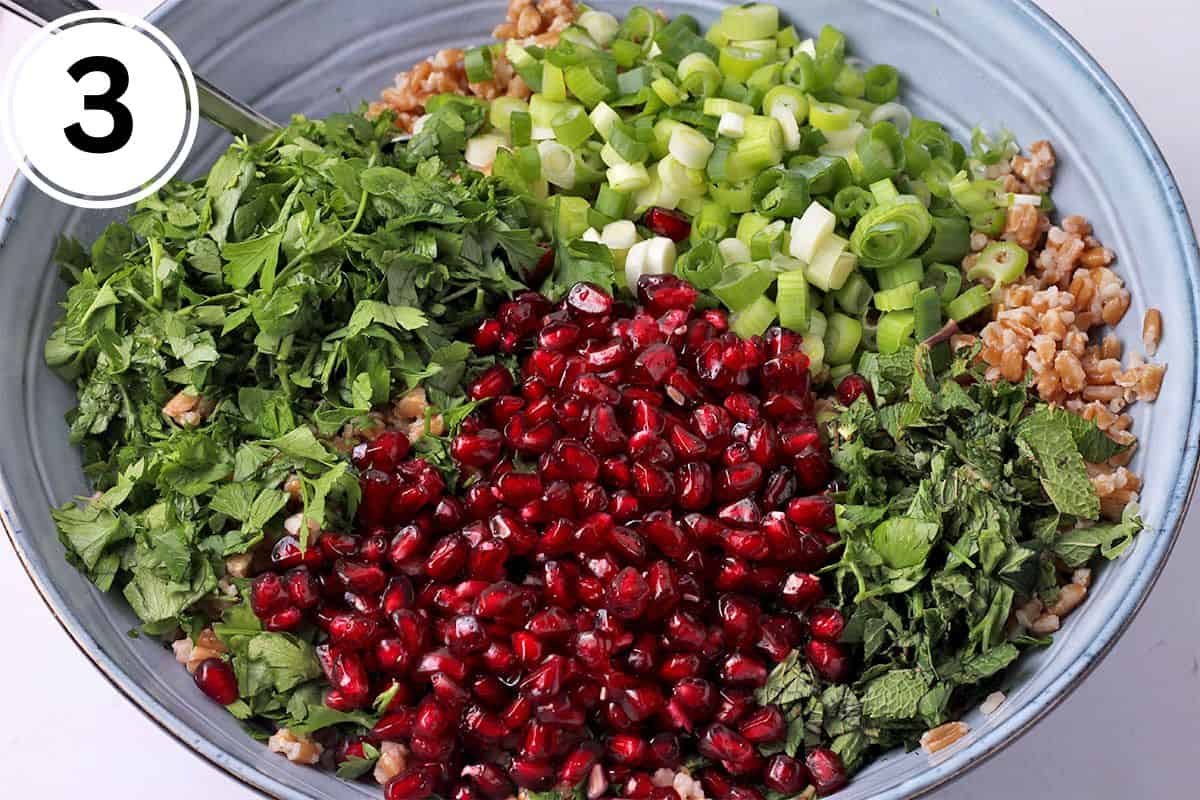 Pomegranate seeds, chopped parsley and mint, green onions, and cooked farro in a blue bowl.