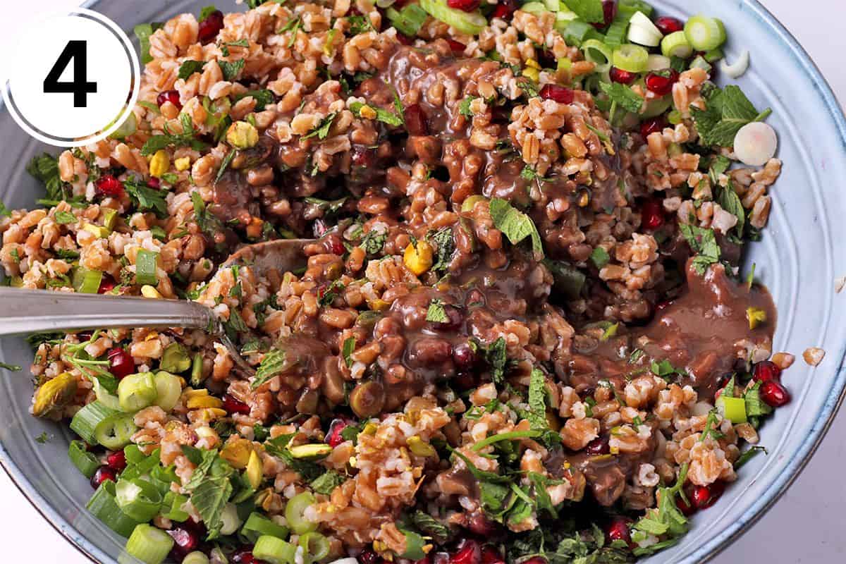 Farro salad with herbs, pomegranate seeds, green onions, and pomegranate dressing is mixed in a bowl.