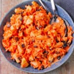A bowl of carrot raisin salad with pineapple and dressing.