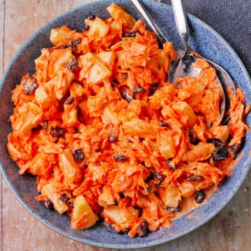A bowl of carrot raisin salad with pineapple and dressing.